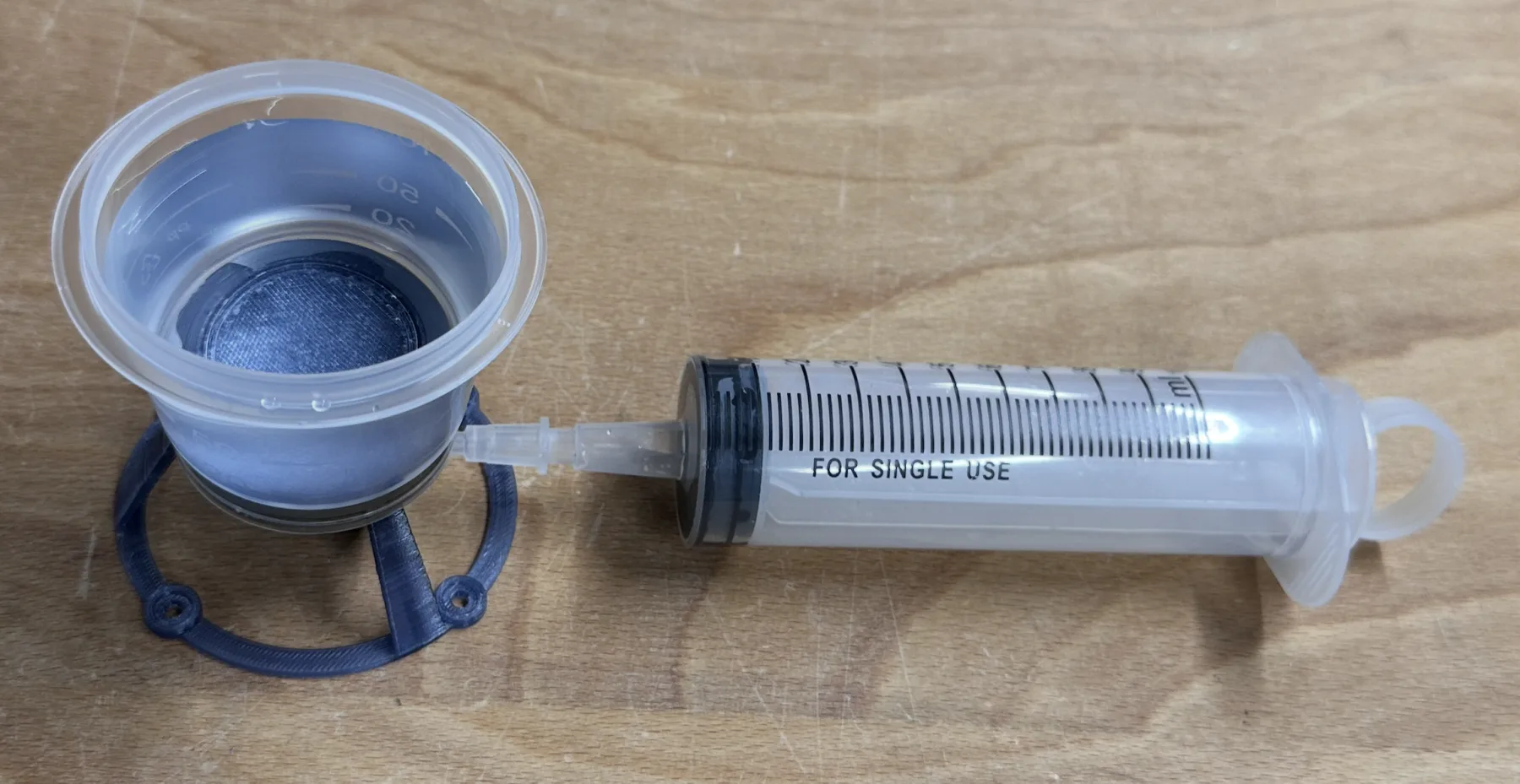 The assembled 3DPLAM manifold mid-filtration: membrane loaded, funnel locked down, syringe attached and drawing the sample through.