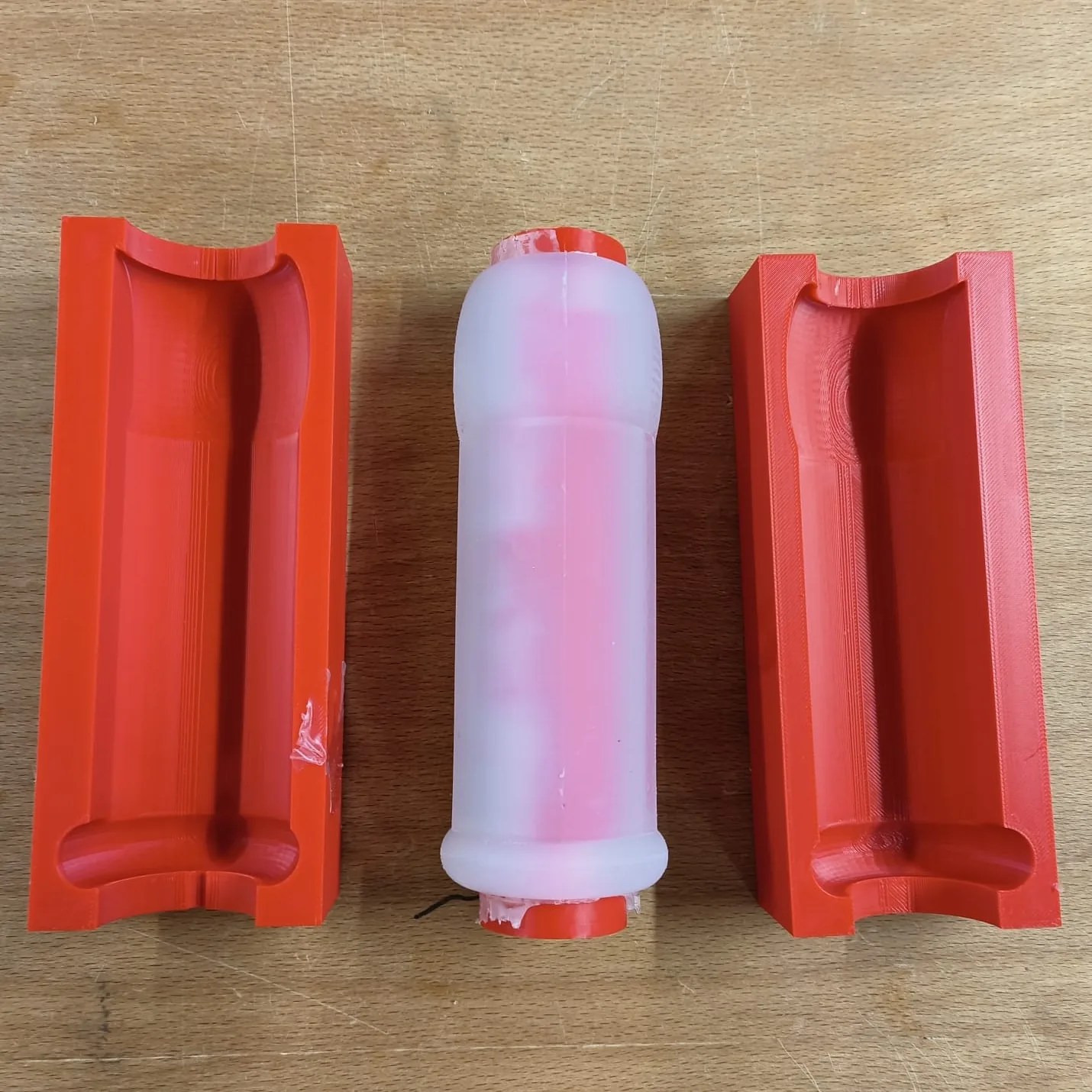 The self-made artificial vagina during demoulding: the cast silicone model on its printed core, with the two outer mould halves opened.
