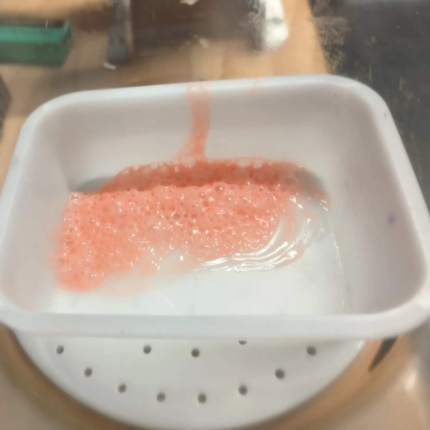 Close-up of orange-tinted silicone foaming with air bubbles as it is degassed under vacuum.