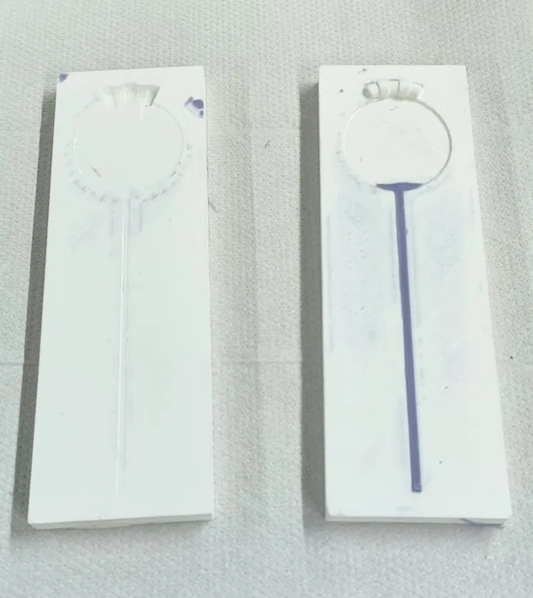 Two flat printed mould halves for the Drawstring lid side by side; frayed, torn silicone is stuck to the top of each cavity, and the right half holds a cast purple string in its channel.