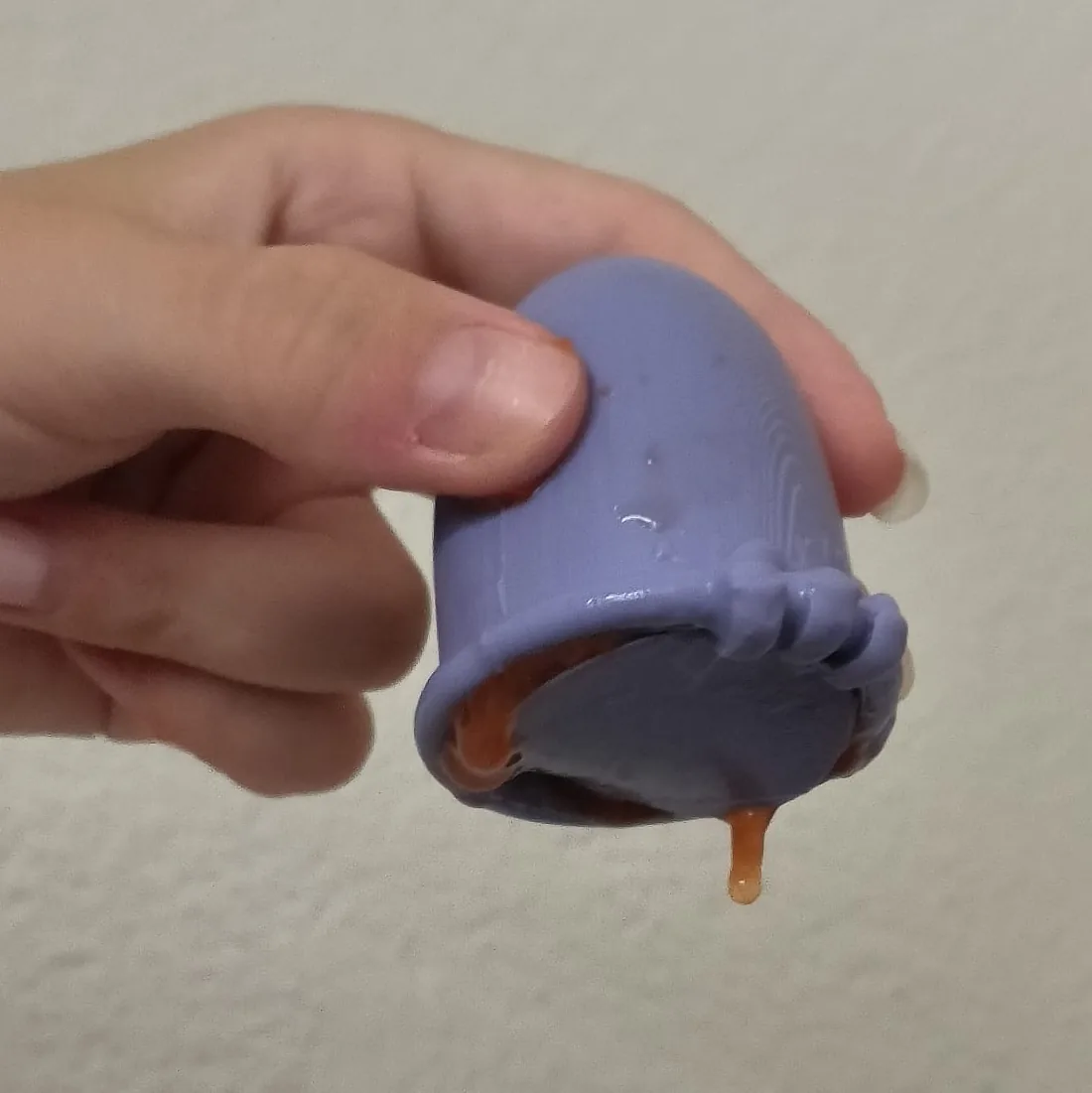 The Drawstring prototype held upside down, its purple lid across the opening: orange test fluid leaking out around the lid’s edge.