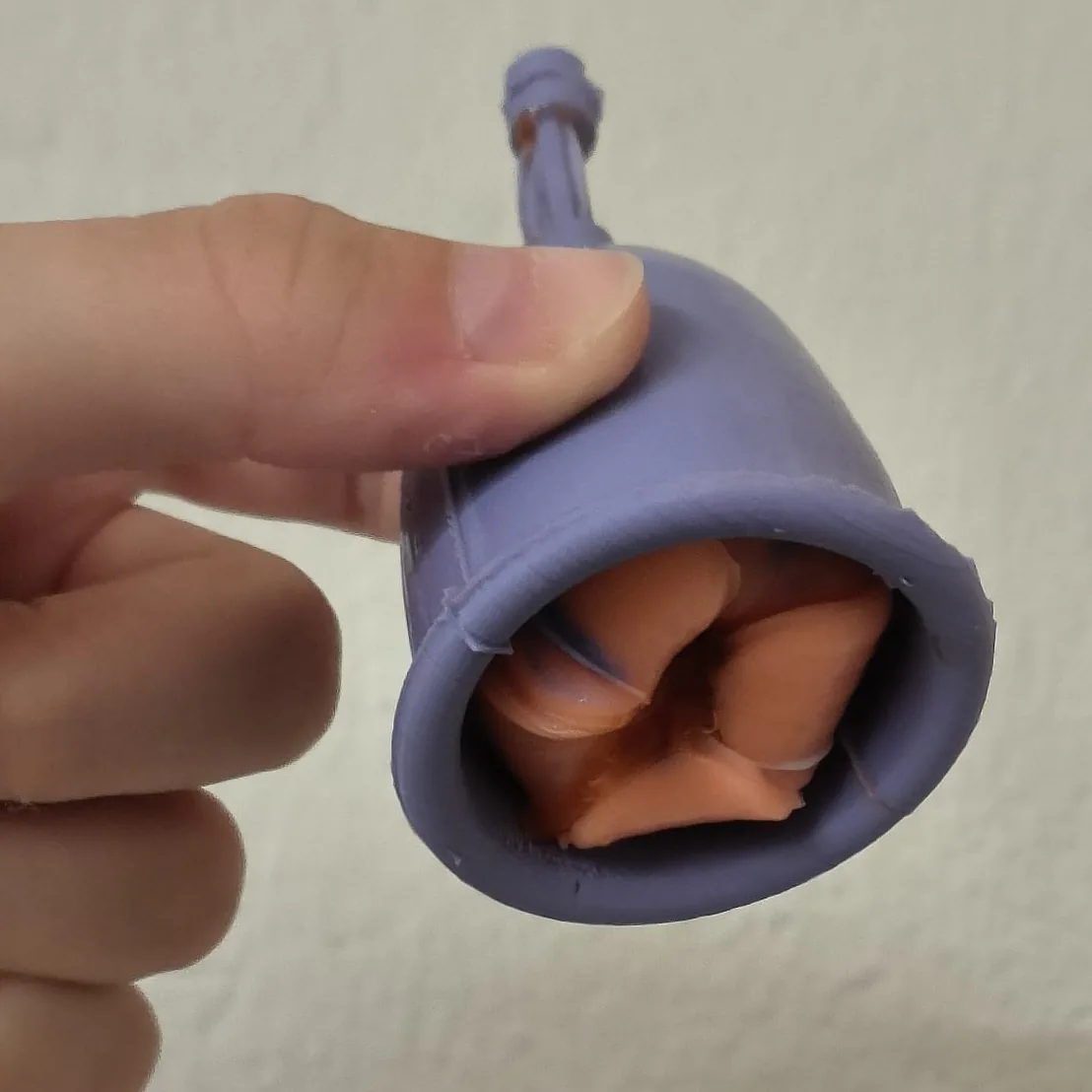 The Flower Low prototype cast in silicone: a purple cup with orange petals inside the rim, held between two fingers.